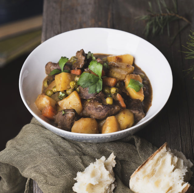 a bowl of traditional irish beef and guinness beer stew with carrots, potatoes and green peas