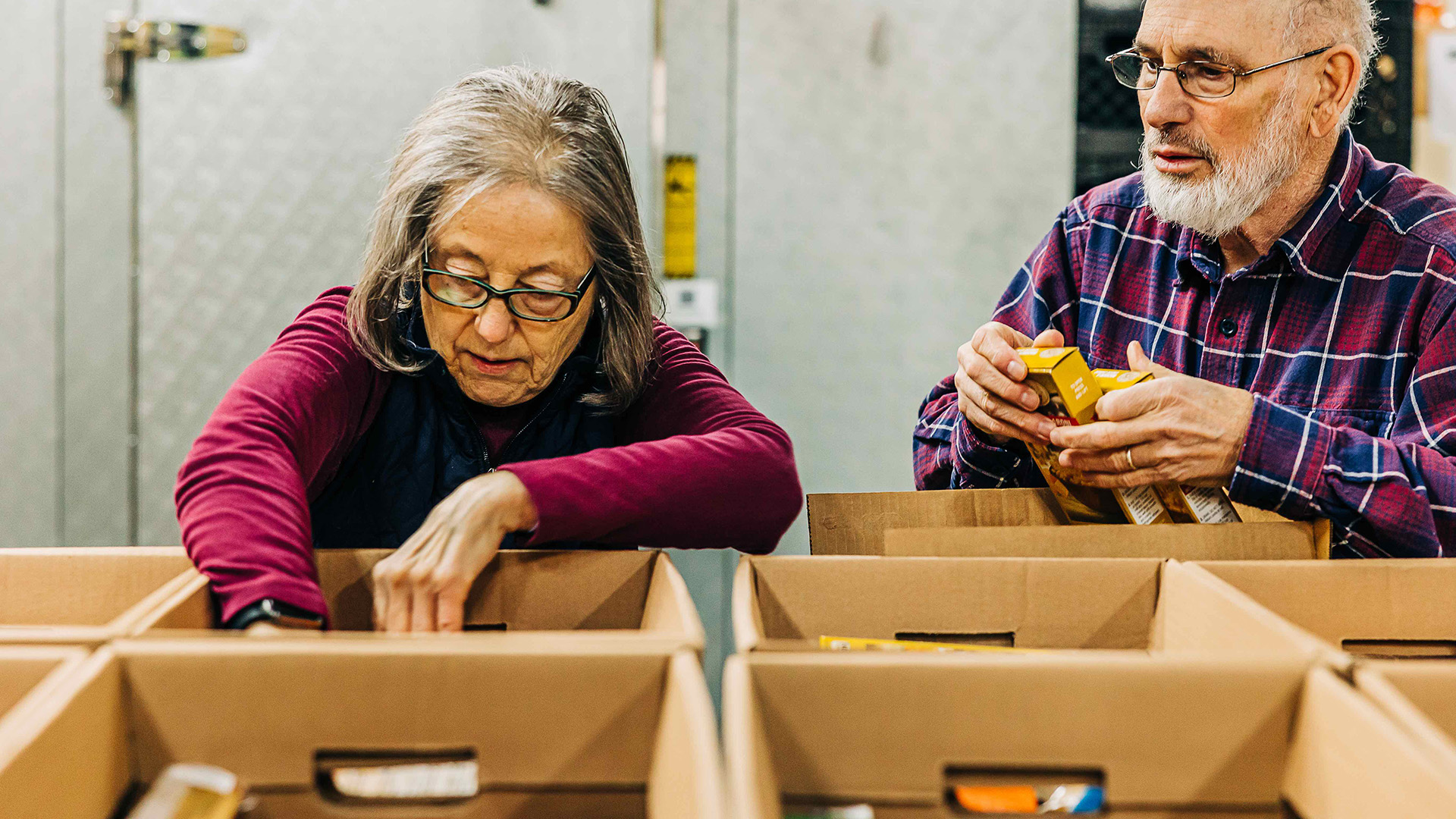 A woman and a man put nonperishable food into donation boxes.