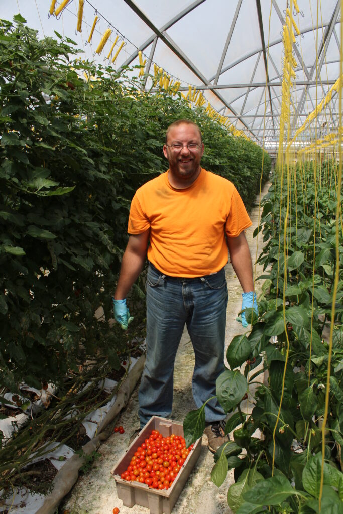 Man in an orange shirt between rows of produce.