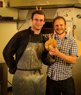 two guys standing next to a large bread making machine