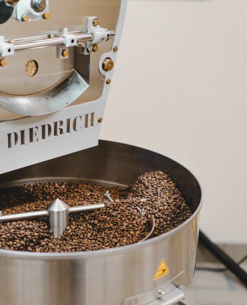 Close-up of a Diedrich coffee roasting machine with freshly roasted coffee beans inside. The metallic machine, gleaming and intricate with its visible mechanical parts, ensures the roasted coffee beans are dark brown and uniformly distributed in the round roasting drum, perfect for Coffee in Duluth.
