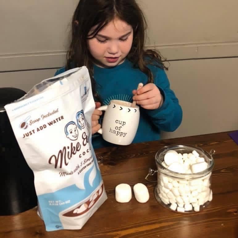 A young girl adds marshmallows to hot cocoa