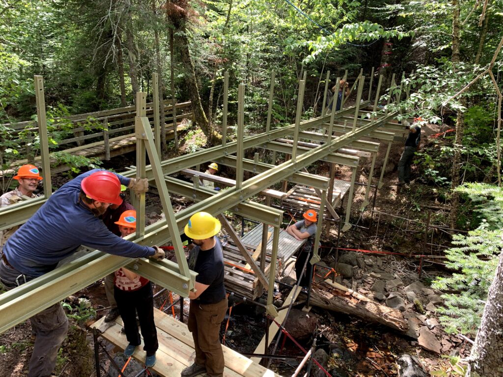 workers adding a bridge to a trail in the forest