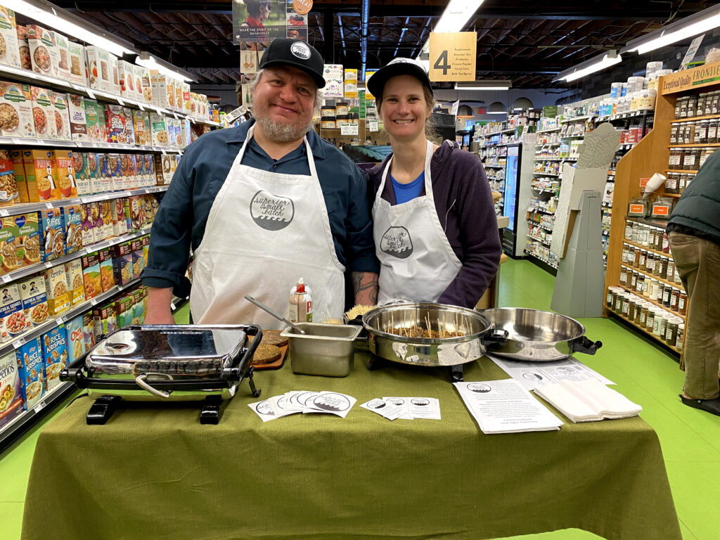 Two individuals stand behind a table at a grocery store