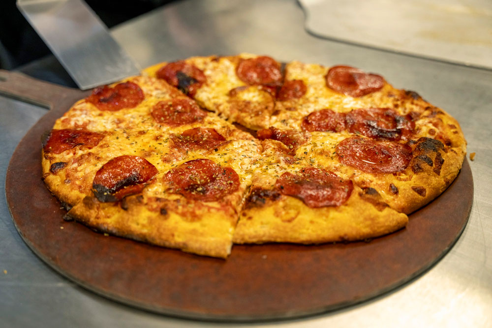 A freshly baked pepperoni pizza on a wooden serving board, with eight slices, is displayed on a countertop. The golden-brown crust is crispy, and the melted cheese is topped with evenly spaced pepperoni slices.