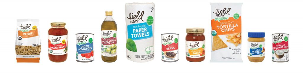 A lineup of Field Day brand products, including a bag of penne pasta, a jar of pasta sauce, a can of diced tomatoes, a bottle of olive oil, a roll of paper towels, a can of black beans, a jar of salsa, a bag of tortilla chips, a box of peanut butter sandwich crackers, and a jar of coconut oil.