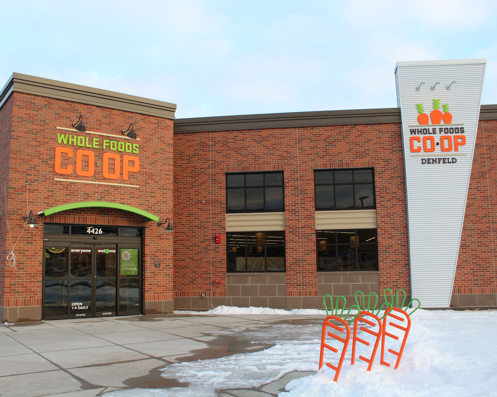 A brick building with large windows houses the Whole Foods Coop Duluth MN. The entrance has an orange awning above the door with 
