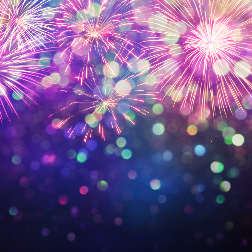 Colorful fireworks burst in the night sky, illuminating the scene with vibrant pink, purple, and green lights. The background fades into a gradient of deep blues and purples, with bokeh light effects creating a festive and celebratory atmosphere perfect for New Year's Eve.
