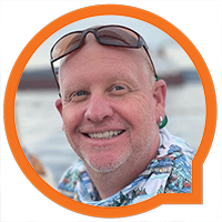 A smiling bald man with a short beard is wearing sunglasses on his head and a colorful shirt. He is framed by an orange circle with a speech bubble design on the bottom right. The background appears to be a body of water.