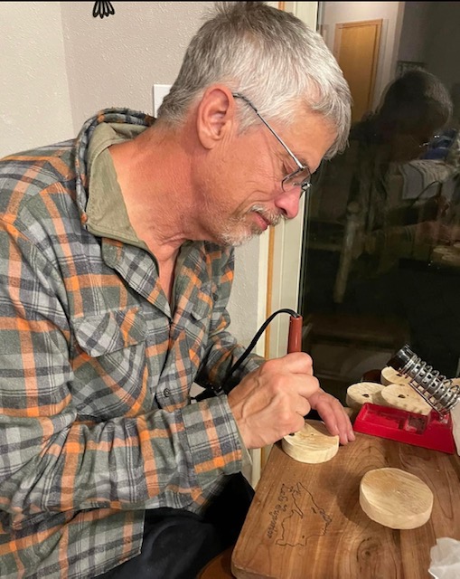 Owner Dale Olson uses a wood burning tool on a wooden candle lid.
