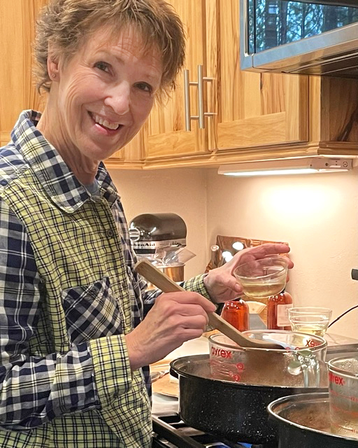 Owner Deedee Olson melts wax in a glass bowl within a pot on a stovetop.