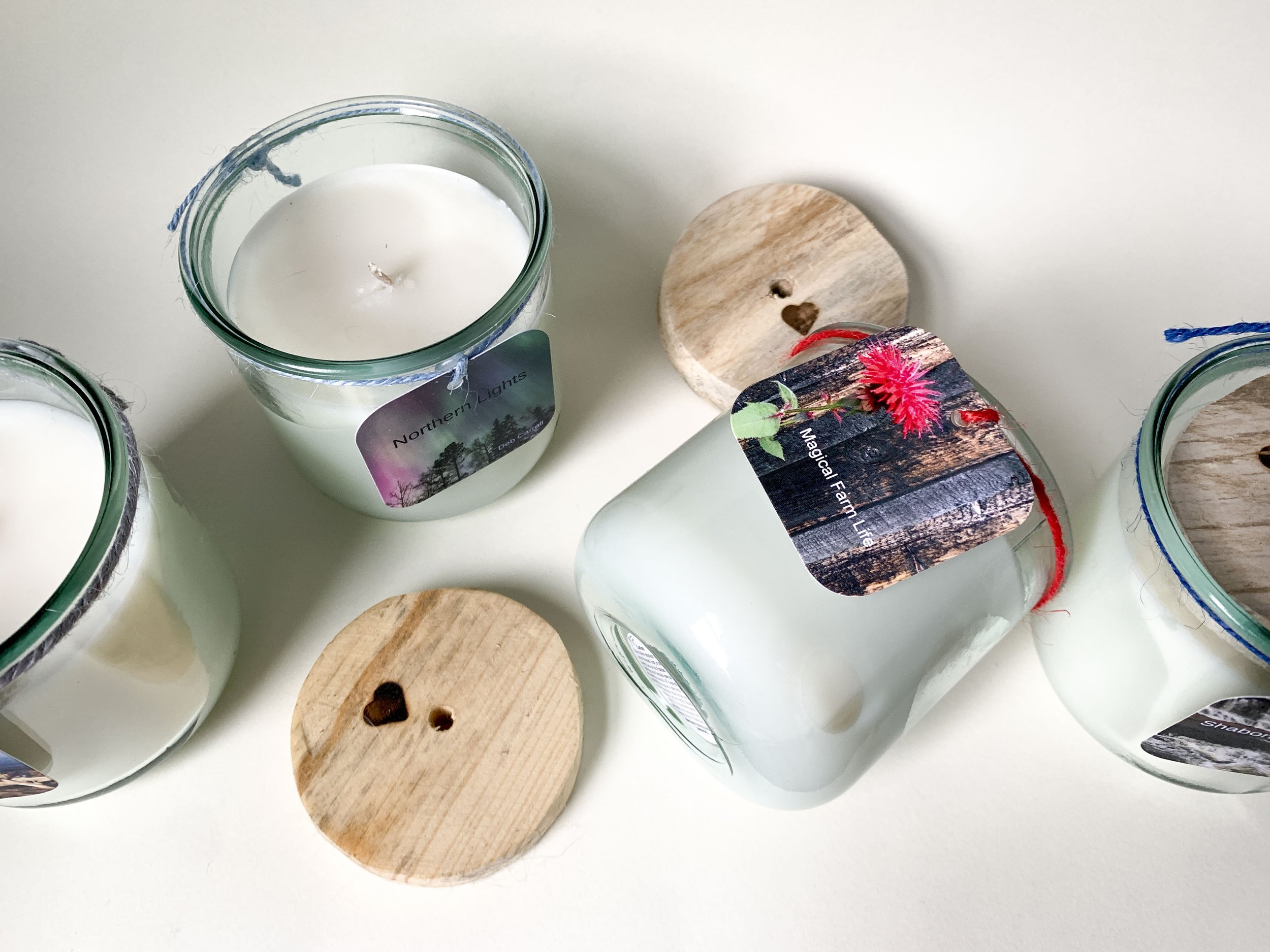Four Hill Farm candles, one is lying on its side, two of the wooden lids are off and lying next to them.