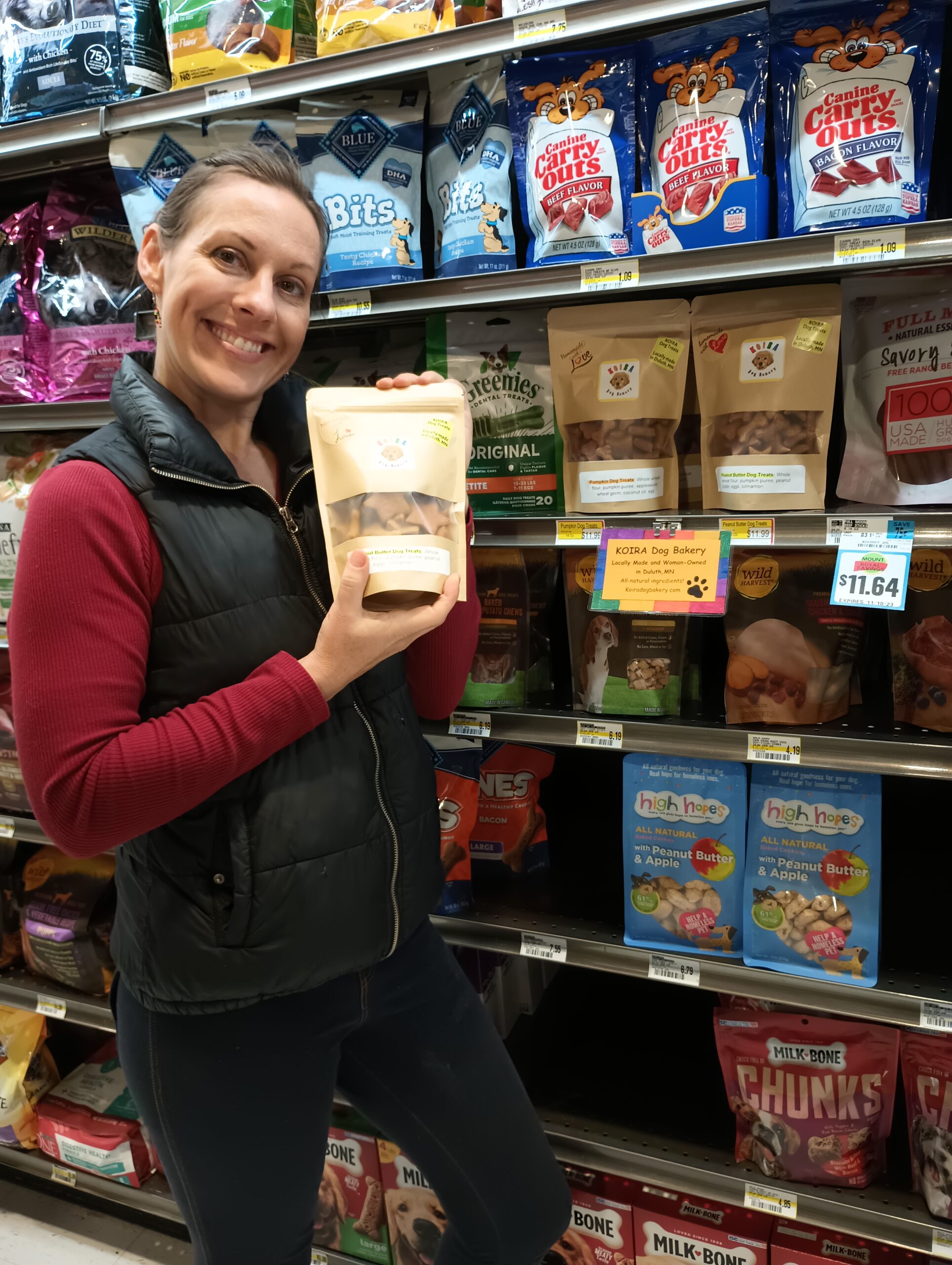 Sarah Carlson, owner of Koira Dog Bakery holding a bag of dog treats in a grocery store.