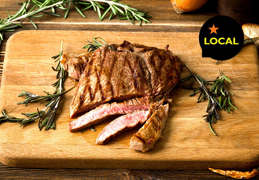 Boneless pork chop partially sliced on a wooden cutting board with rosemary sprigs and the word "Local"