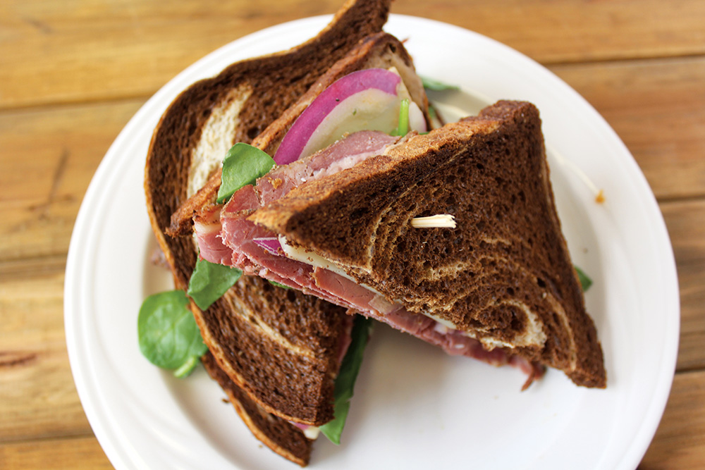 A ham and Swiss sandwich with spinach and red onion on rye bread, cut in half on a white plate.