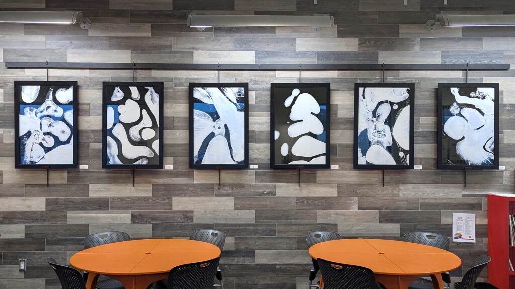 Six large framed photographs of ice formations hang on a gallery rod along the wall in the seating area at the Whole Foods Co-op Denfeld store.