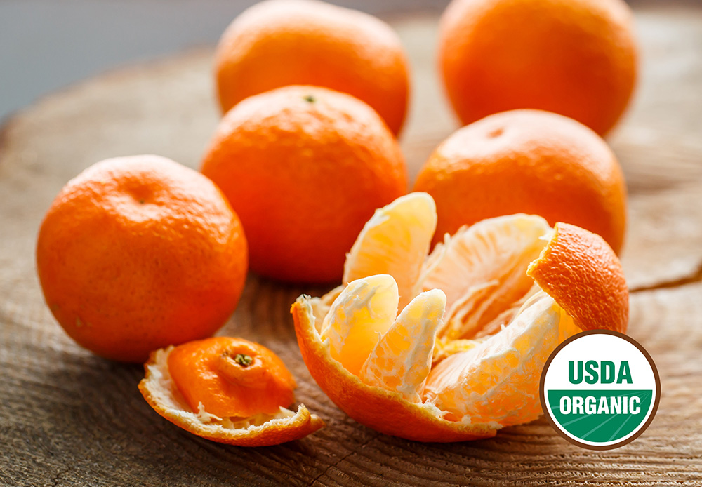 Six mandarins on a wooden board. One is peeled open. USDA organic seal.