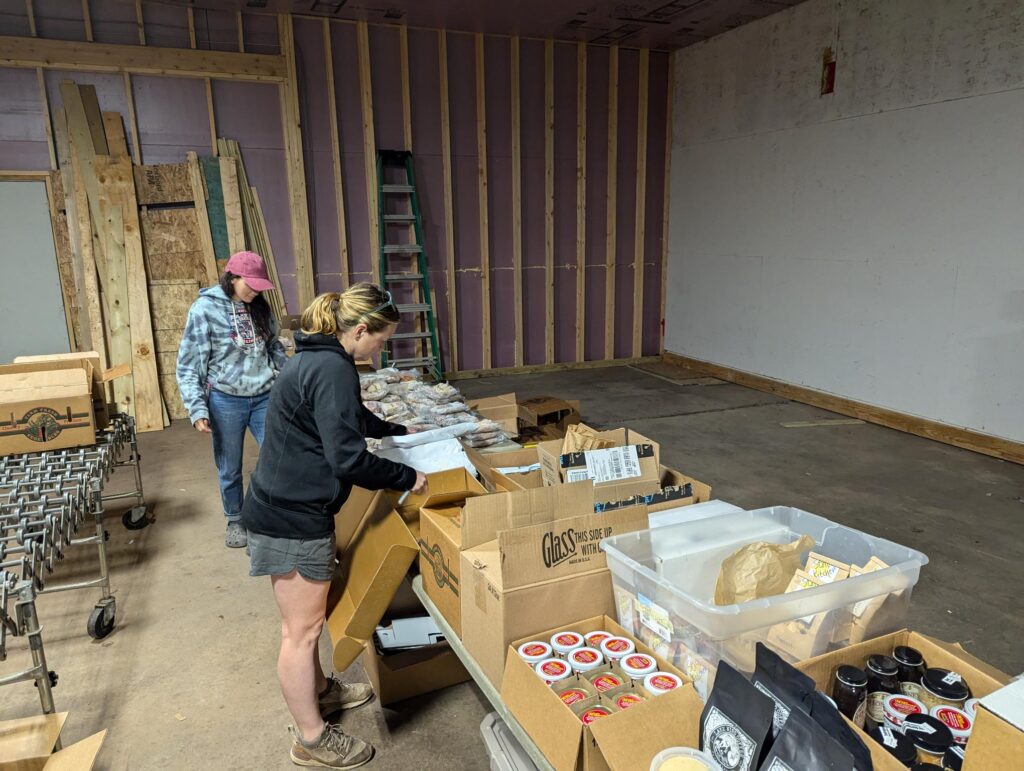 Two people packing boxes on a conveyor in a warehouse.