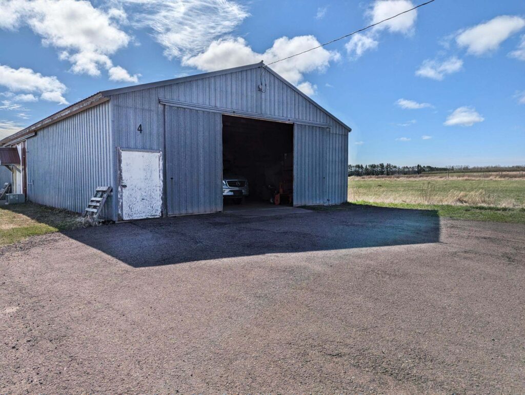 A large warehouse building with a vehicle parked inside. The front bumper, grill, and headlights are visible through the open sliding door.