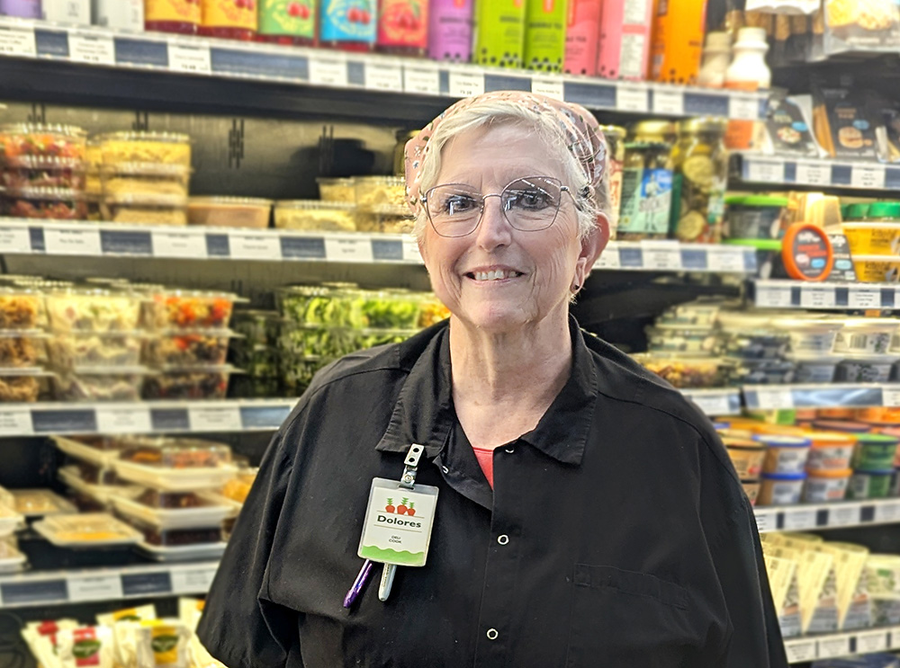 Delores poses smiling in front of the deli grab-n-go case at the Denfeld Whole Foods Co-op.