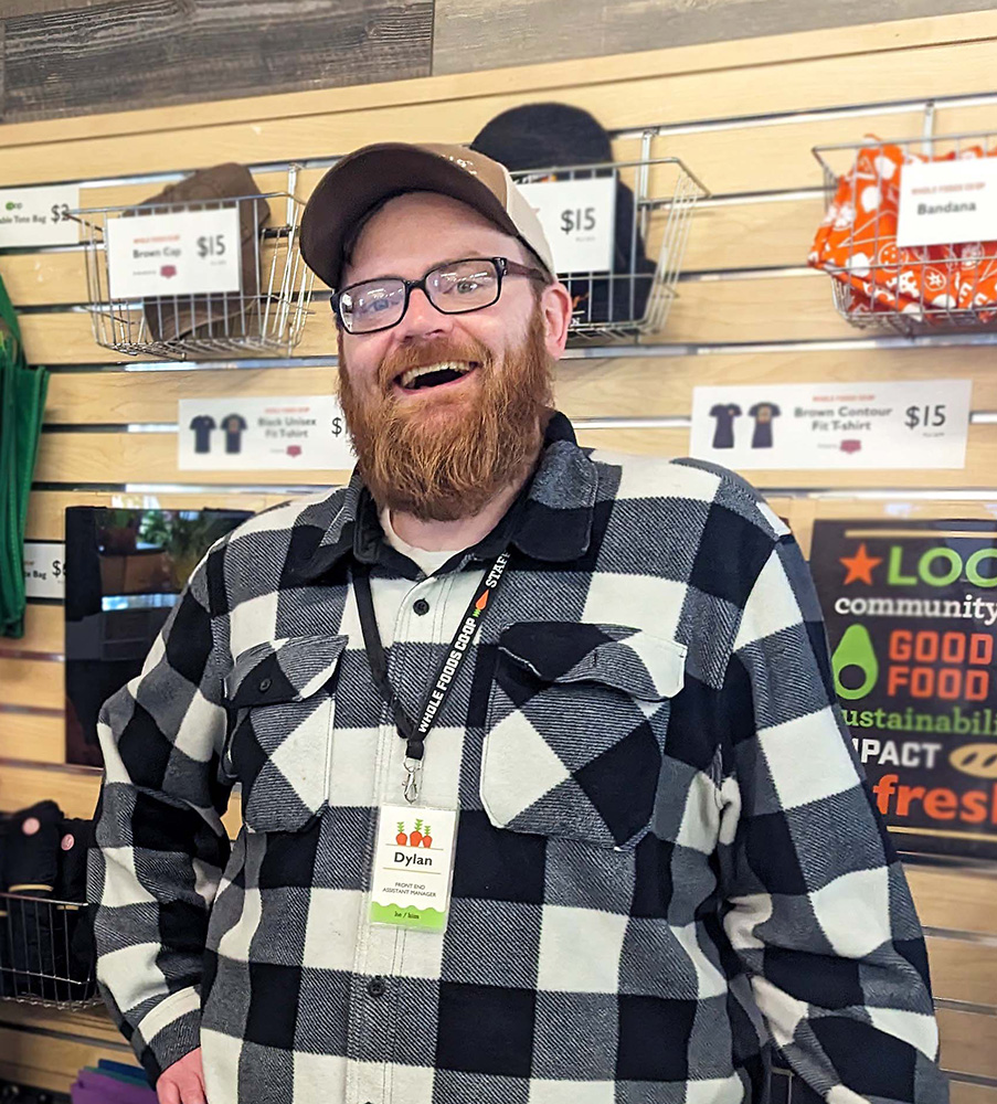 Dylan poses smiling at the customer service counter at the Hillside Whole Foods Co-op.