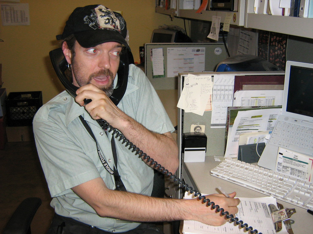 Jim sitting at a desk in an office holding a phone to his ear and writing on a pad of paper.