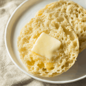 A toasted English Muffin with butter on a white plate.